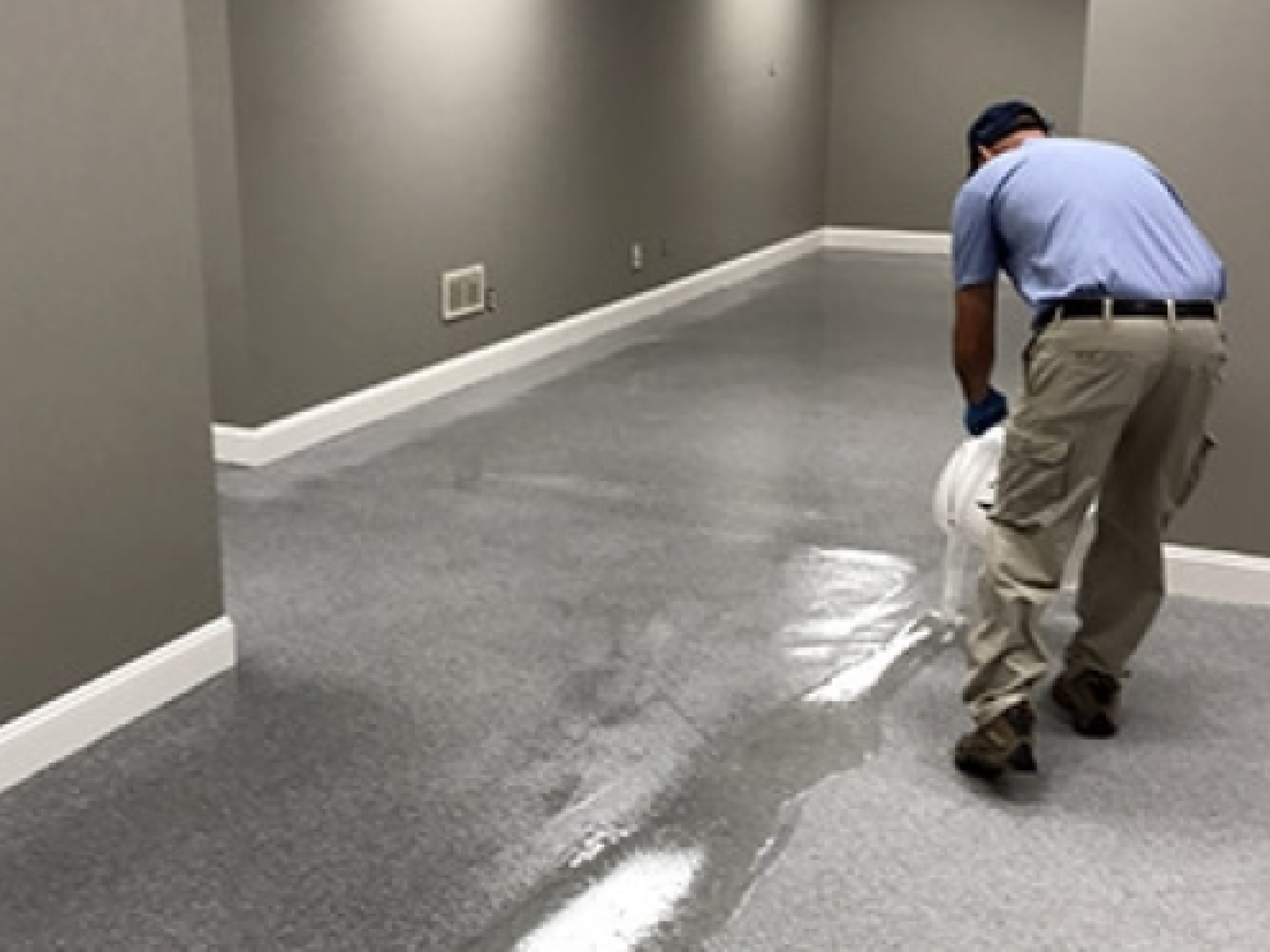 Worker smoothing freshly poured self-leveling cement over a concrete floor.